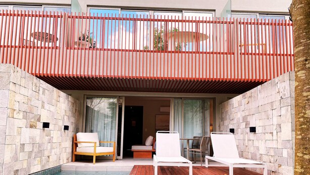Un espace aménagé au bord de la piscine, doté d’une terrasse en bois, de chaises longues blanches et d’un balcon vitré avec une rambarde rouge.
