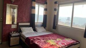 A hotel room with a bed, a nightstand, a mirror, and a window with curtains. - 2 BHK Banglow (Mahabaleswer)