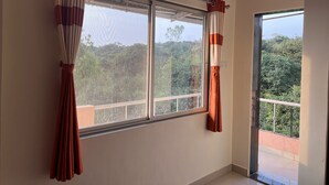 A room with a large window, curtains, and a view of greenery outside. - 2 BHK Banglow (Mahabaleswer)