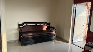 A room with a sofa against a wall, a bed with a red blanket, and a sliding glass door leading to an outdoor area. - 2 BHK Banglow (Mahabaleswer)