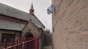 A narrow alleyway with a stone building on one side and a red metal fence. - 1-bed Apartment Sleeps 2 -free Parking -wifi & Tv (Dundee)
