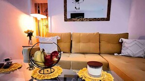 A living room with a sofa, a coffee table with a fruit bowl and a candle, and a lamp. - 1-bed Apartment Sleeps 2 -free Parking -wifi & Tv (Dundee)