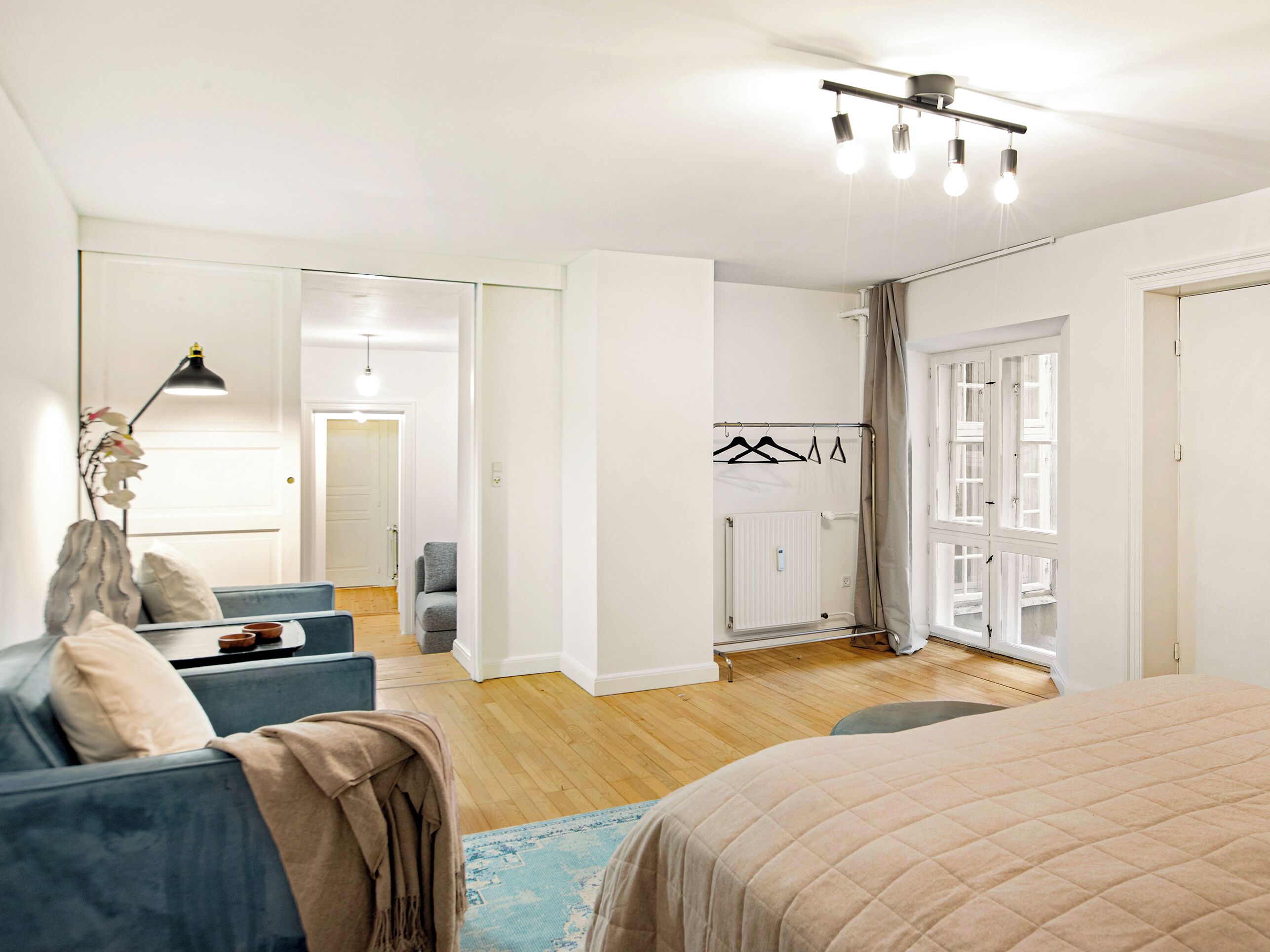 A modern bedroom with a large bed, a sofa, a desk, and a radiator.