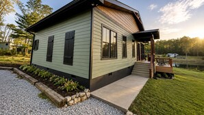 A modern single-story house with a covered porch and a small deck, surrounded by a well-maintained lawn and a gravel driveway. - Lake Therapy at The Retreat at Water's Edge (Tracy City)