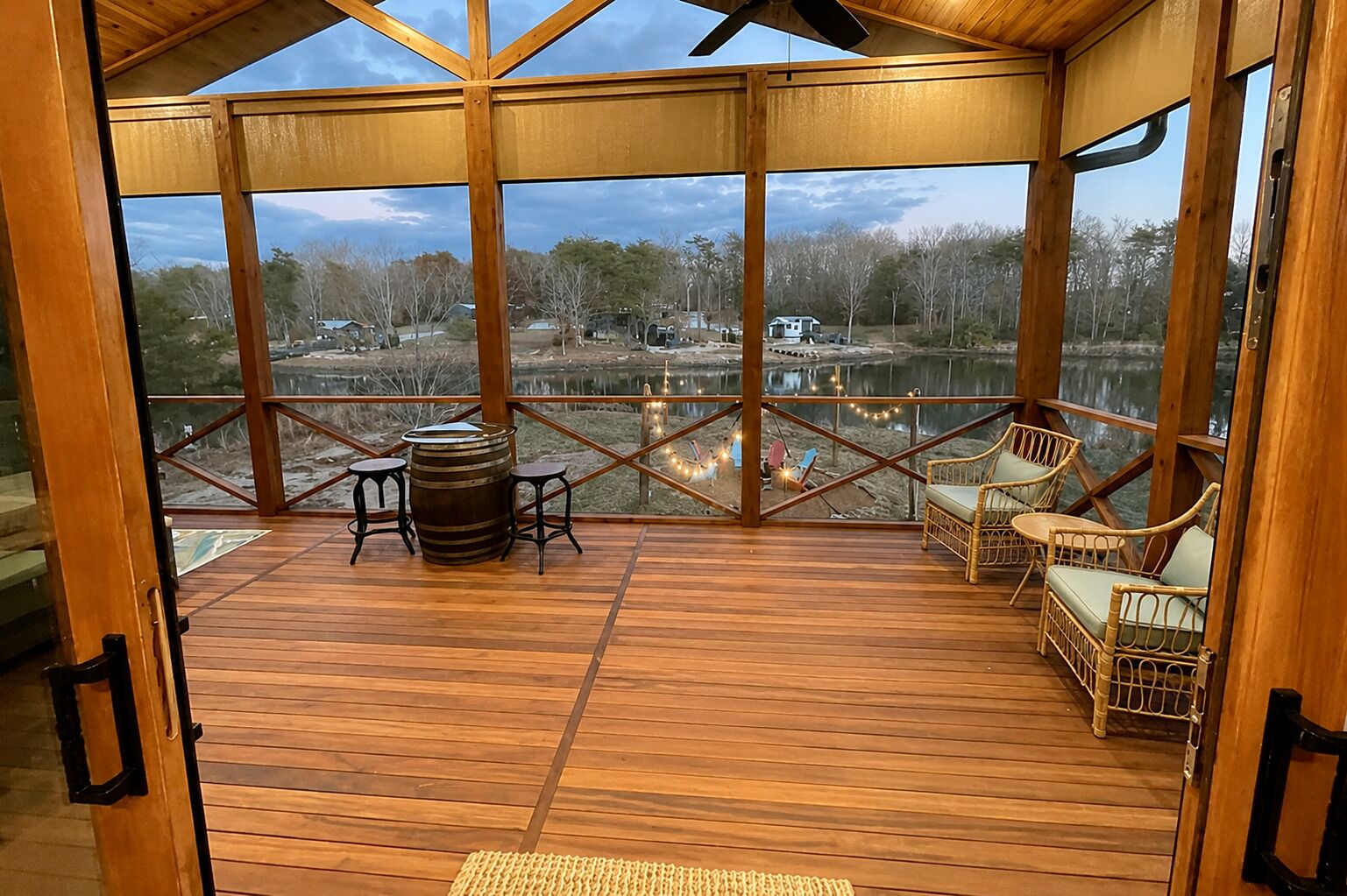 Une terrasse en bois offrant une vue sur un lac, avec un tonneau et des meubles en osier.