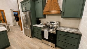 A kitchen with green cabinets, stainless steel appliances, and a wooden hood. - Lake Therapy at The Retreat at Water's Edge (Tracy City)