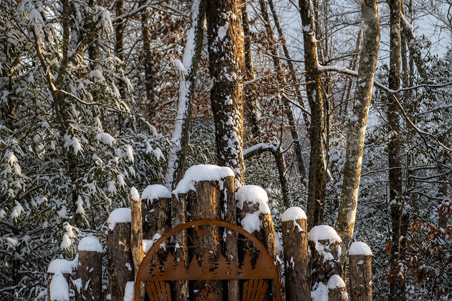 A wooden fence with snow accumulation, surrounded by a forested area.