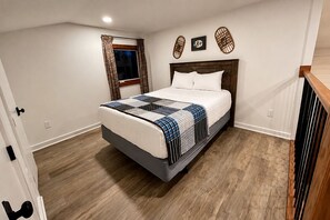 Un dormitorio con cama, suelo de madera, una ventana con cortinas y adornos en la pared.