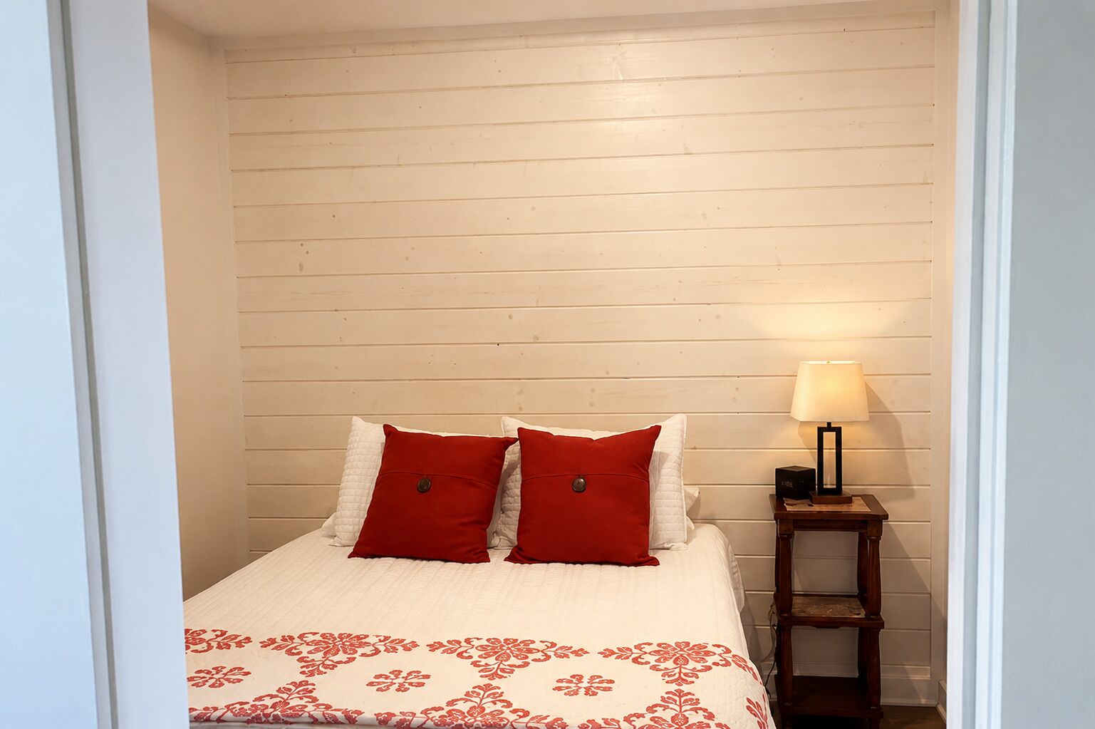 A bedroom with a bed, two pillows, a bedside table with a lamp, and a patterned bedspread.