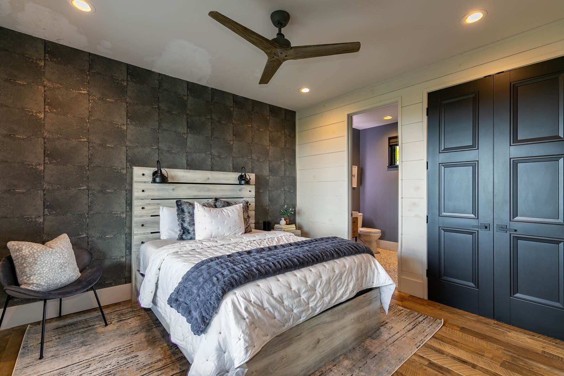 Ein Schlafzimmer mit einem Holz-Kopfteil, einem Bett mit himmelblauer Bettdecke, einem dunklen Holzboden und einer dunklen Tür.