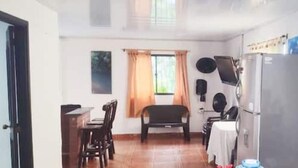 Una cocina compacta con refrigerador, una mesa de comedor con sillas y una ventana con cortinas.