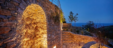 An ancient stone structure with an arched doorway, a stone staircase, and a view of the sea.