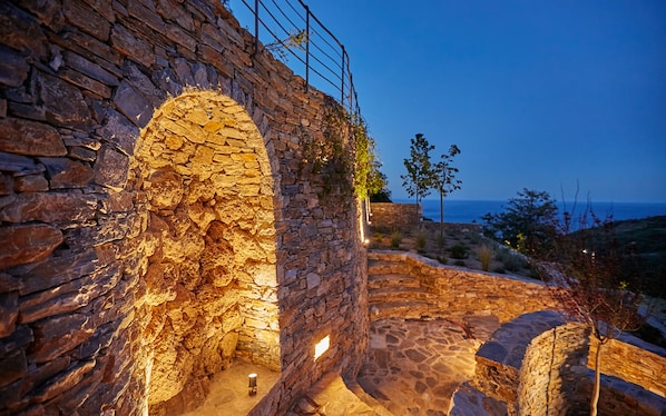 An ancient stone structure with an arched doorway, a stone staircase, and a view of the sea.