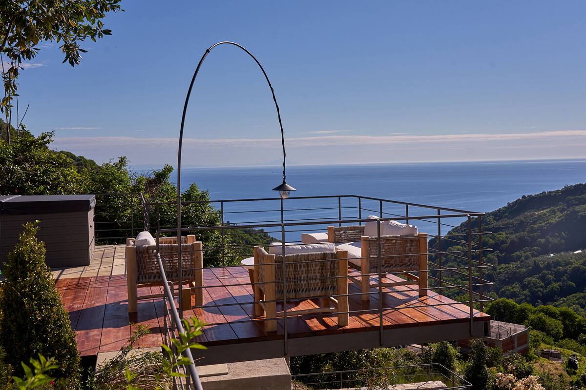 A terrace with wicker furniture, a lamp, and a view of the sea.