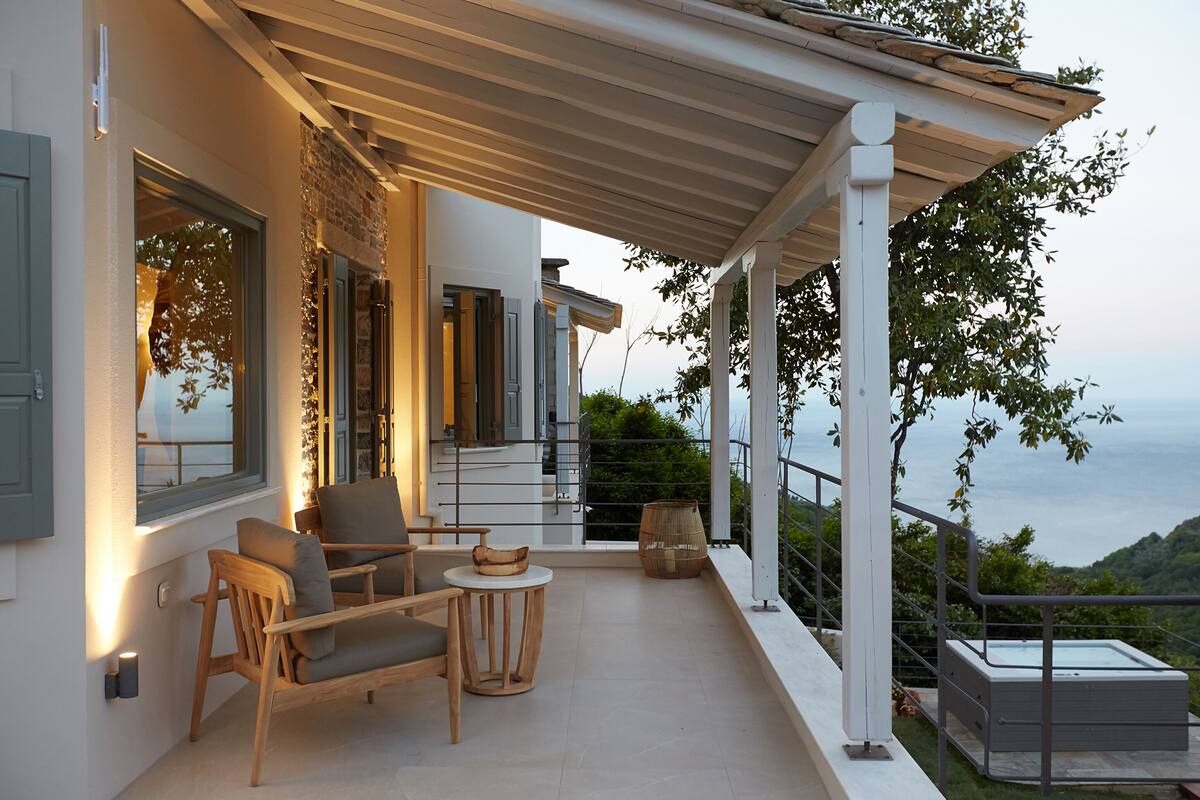 A balcony with a wooden chair and table, a hot tub, and a view of the sea.