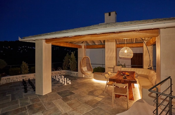 Un patio al aire libre con un tablero de ajedrez, una mesa de madera y una silla de mimbre.