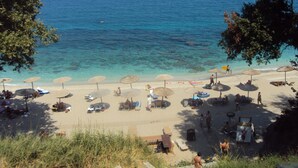 A beach with clear blue water, umbrellas, and people. - Sunrise Garden Hills (Zagora-Mouresi)