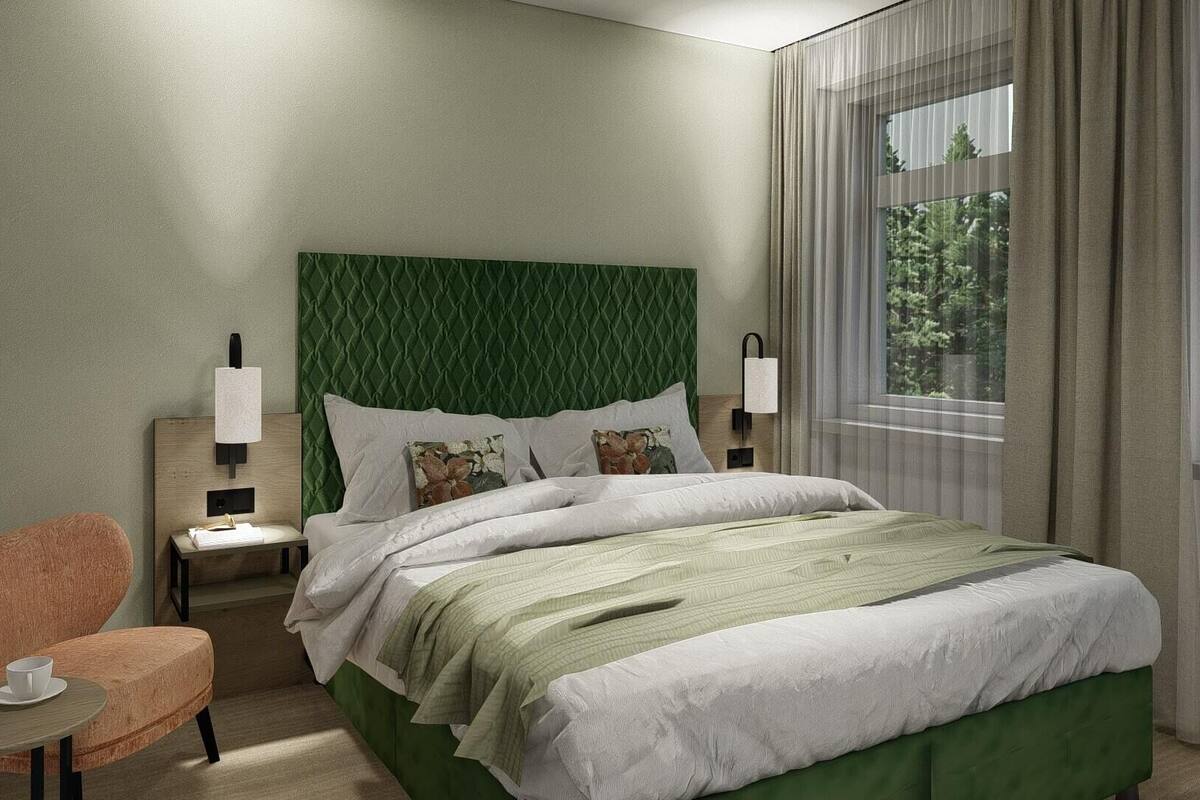 Quarto de hotel com cabeceira estofada verde, cama com roupa de cama branca, pequena mesa de cabeceira de madeira com xícara e pires, poltrona estofada verde e janela com cortinas.