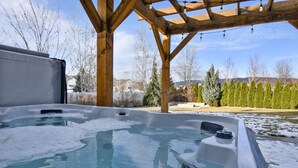 A hot tub under a wooden pergola with a clear view of trees and mountains in the background.