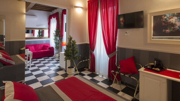 A hotel room with a checkered floor, red and white decor, a television, and a small Christmas tree. - Suite Apartment 2/4 Persons (Firenze)