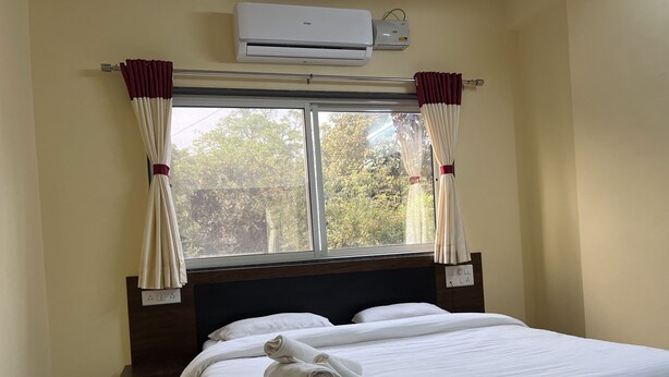 Habitación de hotel con cama, ropa blanca, aire acondicionado y ventana con cortinas.