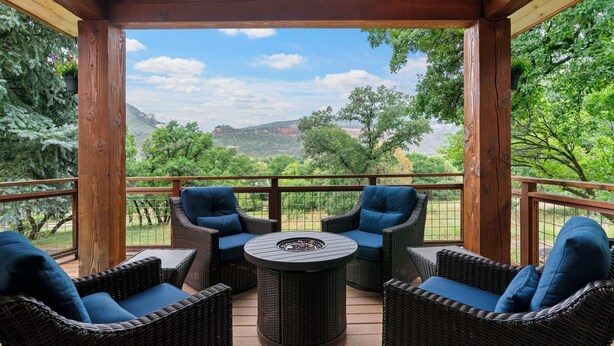 Uma área de estar coberta ao ar livre, com móveis de vime e uma mesa central, com vista para uma paisagem deslumbrante.