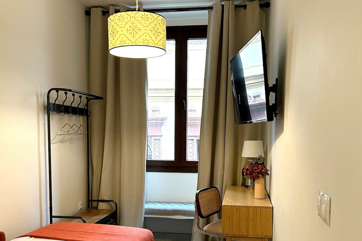 Una habitación de hotel con una cama, un escritorio con una silla, un televisor y una ventana con cortinas.