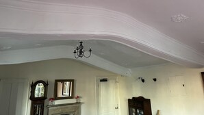 Une pièce avec un plafond haut, des moulures décoratives, un lustre, une cheminée et un miroir.