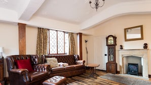 Un salon traditionnel avec un canapé en cuir, un plancher en bois, une cheminée et une horloge comtoise.