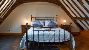 Une chambre à coucher avec un plafond voûté, un cadre de lit en métal, deux tables de chevet avec des lampes et une fenêtre laissant entrer la lumière naturelle.