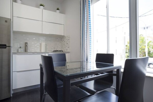 A modern kitchen with white cabinets, a glass table, and two black chairs. - Miami Beach Getaway 100 yards from Beach (Miami)