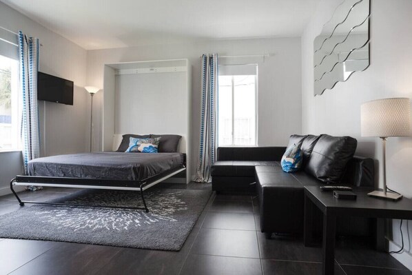 A modern bedroom with a bed, a sofa, a desk, and a TV.