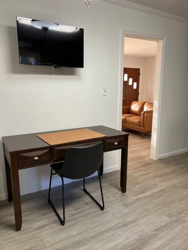 A room with a wooden desk, a black chair, and a mounted flat-screen TV.