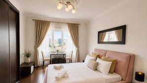 Habitación de hotel con una cama grande, un escritorio con sillas, una ventana con cortinas y vistas a la ciudad.