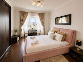 A hotel room with a large bed, a desk with chairs, a window with curtains, and a city view.