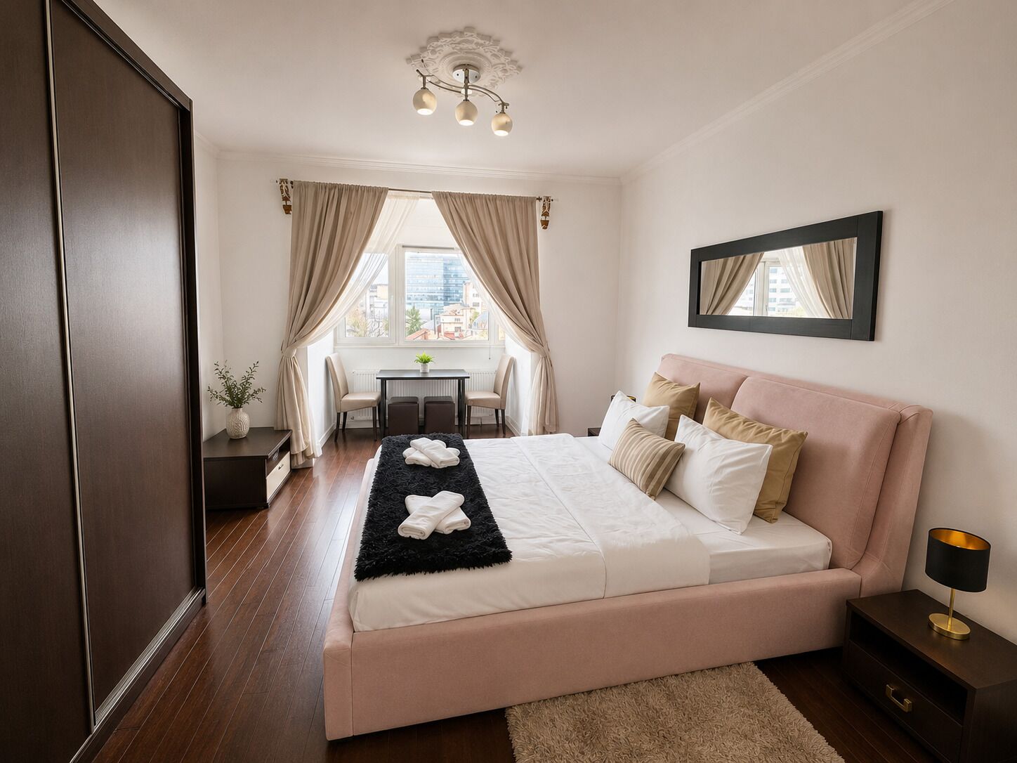 Un dormitorio con cama, escritorio y silla, una ventana con cortinas y vistas a la ciudad.