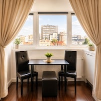 A room with a window, a table with two chairs, a bench, and a potted plant.