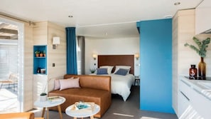 A modern hotel room with a brown sofa, a small round table, a bed with a wooden headboard, and a blue accent wall. - Camping Tikayan les Cigales le Muy (Le Muy)