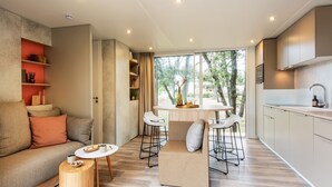 Un espace de vie moderne et compact comprenant un canapé, une petite table ronde, un coin repas avec deux tabourets de bar et une cuisine équipée d’un évier et de placards.