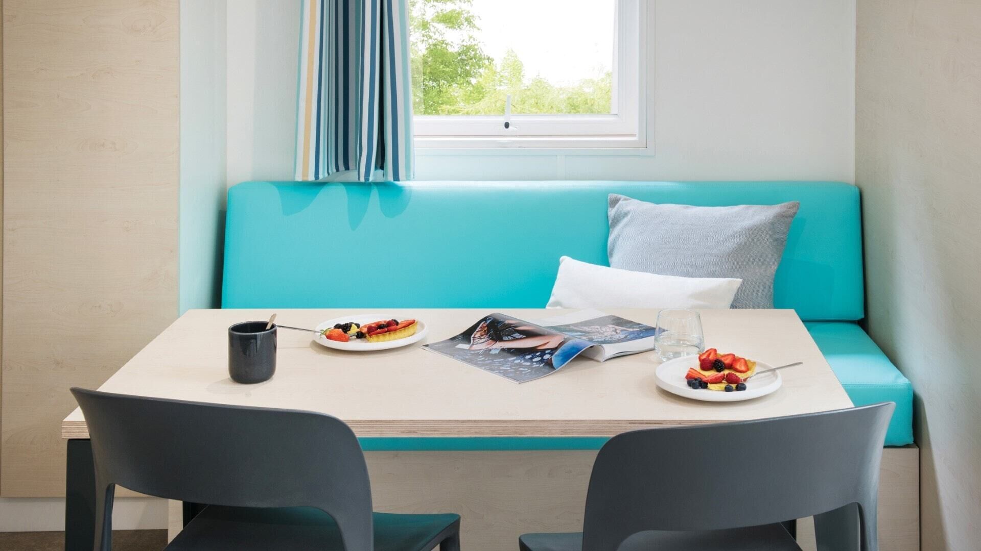 Een gezellige kamer met een blauwgroene bank, een klein tafeltje met een tijdschrift, een schaal fruit en een mok.