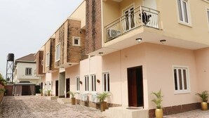 Uma fileira de casas geminadas de dois andares com varandas, um pátio pavimentado e plantas em vasos.