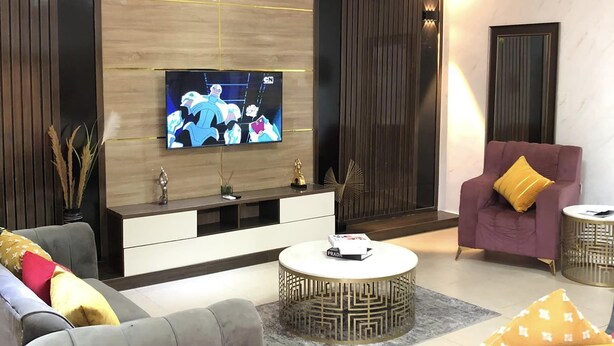 Uma sala de estar moderna com televisão de tela plana, sofás cinzas, uma mesa de centro redonda e uma poltrona roxa.