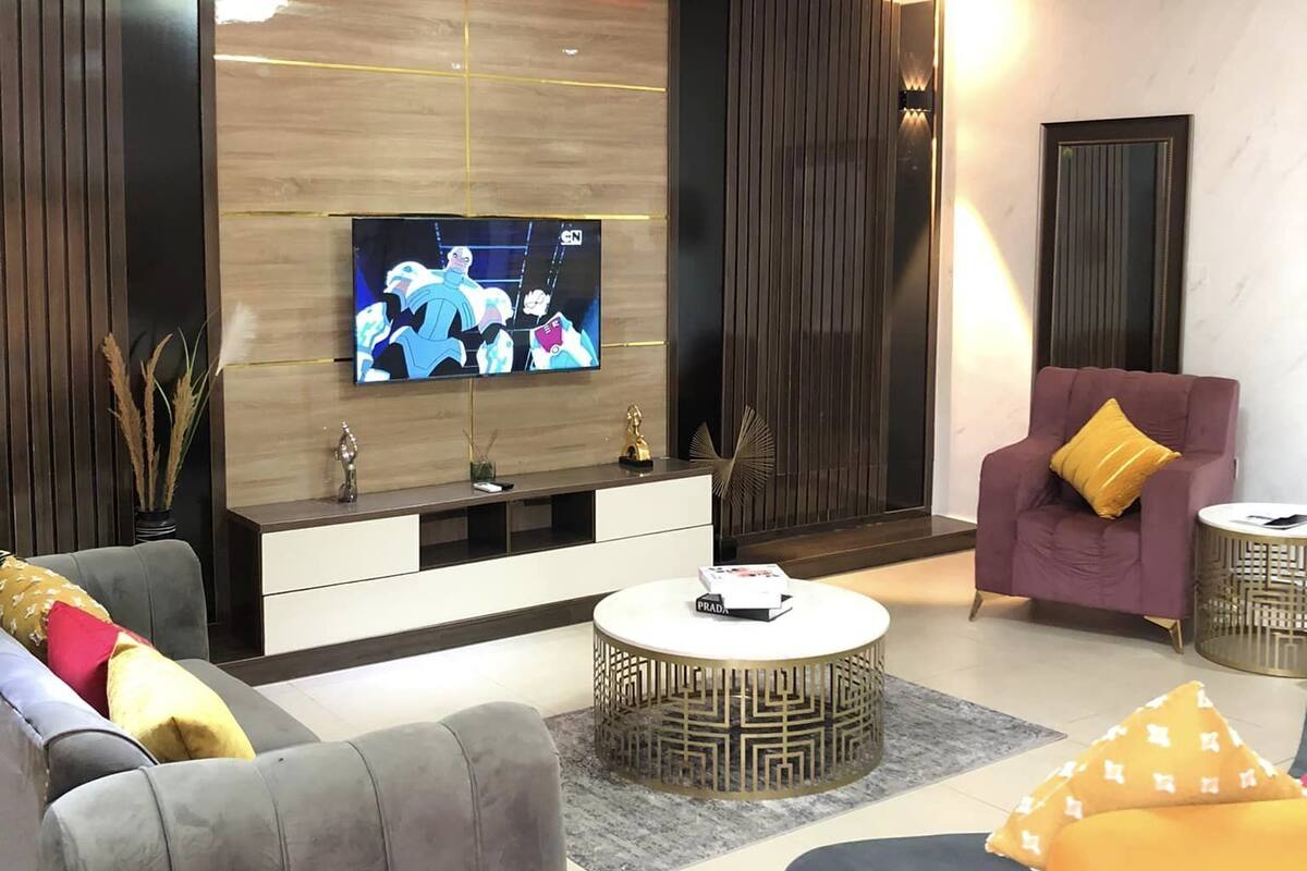 Een moderne woonkamer met een flatscreen televisie, grijze banken, een ronde salontafel en een paarse fauteuil.