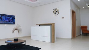 Um hall de hotel moderno com design minimalista, apresentando uma grande TV de tela plana, uma obra de arte única na parede e uma área de estar com uma poltrona.