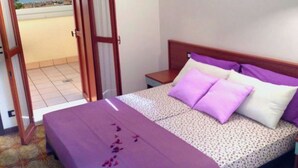 A bedroom with a bed, a nightstand, and a view of the beach through an open door. - Elegant two Story Apartment Near the Beach (San Michele al Tagliamento)