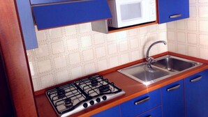 A kitchen with blue cabinets, a white microwave, a stainless steel sink, and a gas stove. - Elegant two Story Apartment Near the Beach (San Michele al Tagliamento)