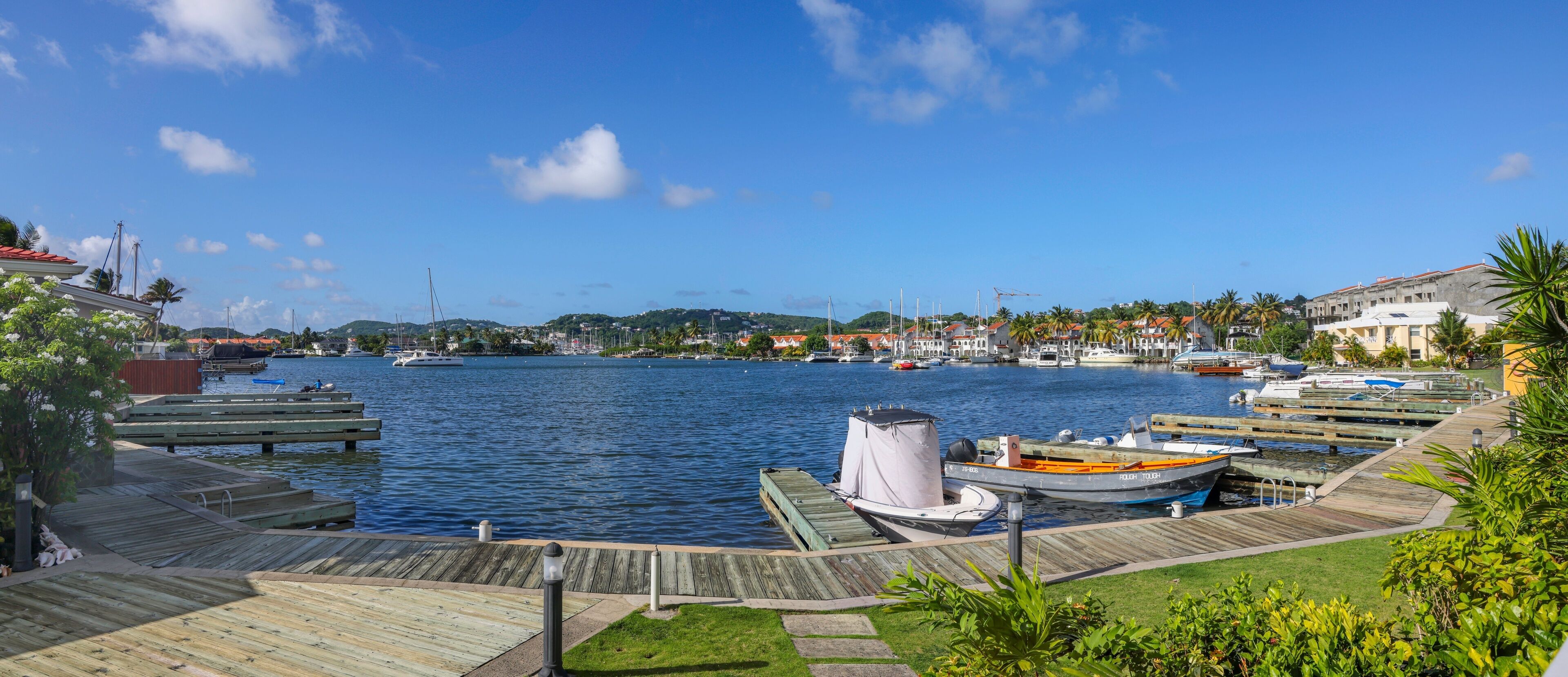 A marina with docked boats, a wooden walkway, and a view of a town across the water.