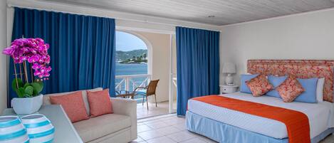 Quarto de hotel com cama, sofá, mesa com objetos decorativos e vista para o mar.