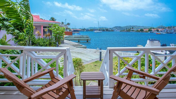 A wooden deck with two chairs and a small table, overlooking a marina with boats and a distant cityscape. - The Harbour #6 - 3 Bedrooms in Rodney Bay 3 Townhouse by RedAwning (Gros Islet)
