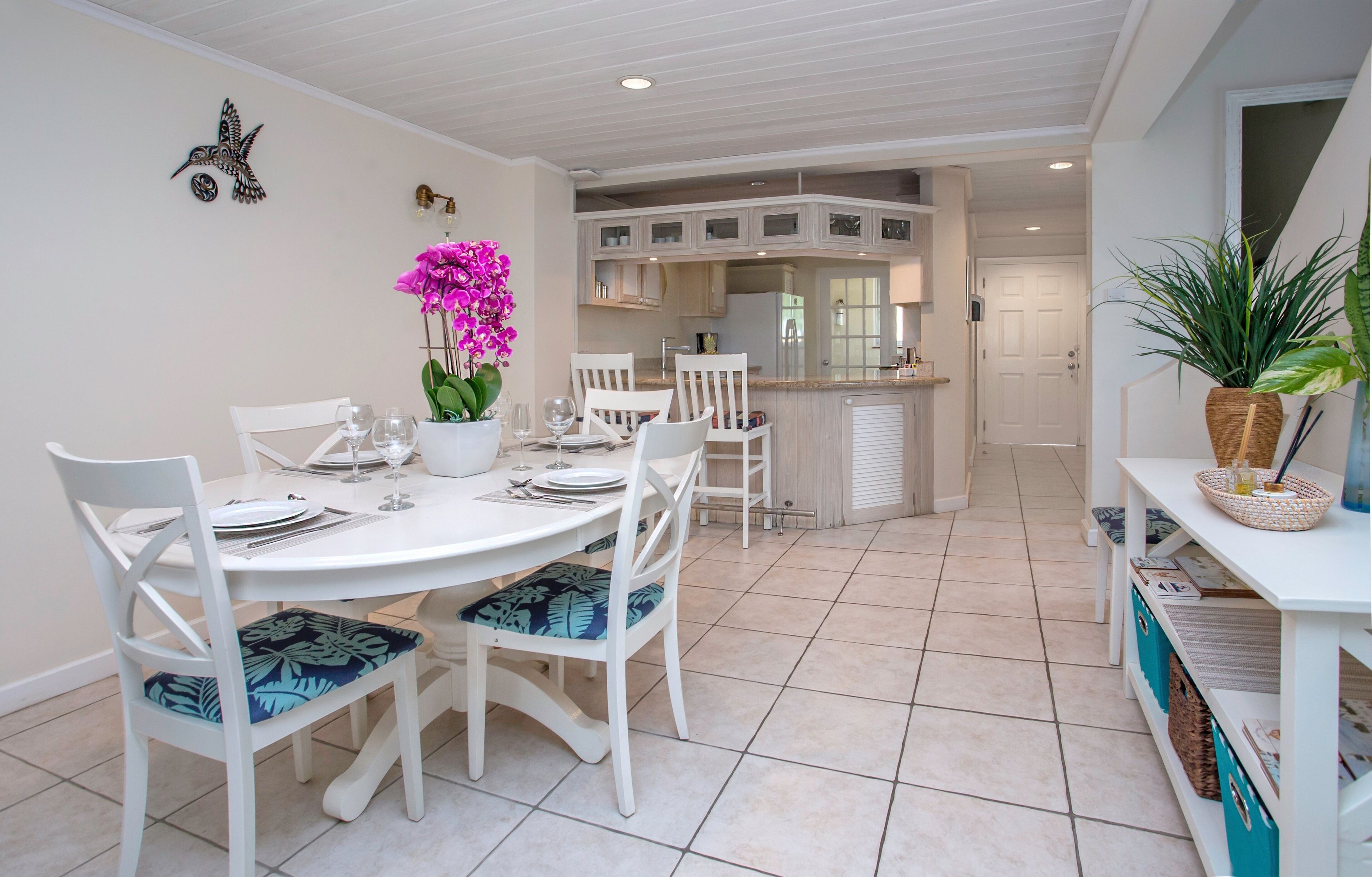 A dining area with a white table and chairs, a potted orchid, and a kitchen in the background.